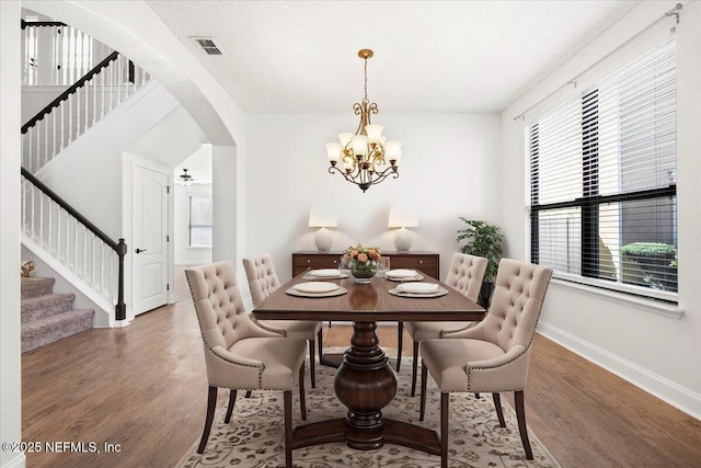 dining room featuring wood finished floors, visible vents, baseboards, arched walkways, and stairs