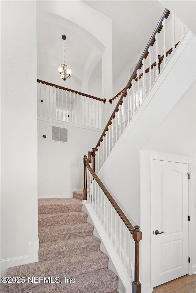 staircase with a notable chandelier, visible vents, a high ceiling, and baseboards