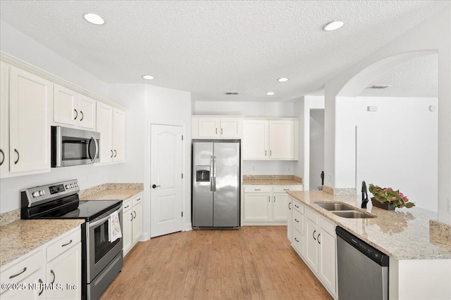 kitchen featuring light wood-type flooring, a sink, light stone counters, white cabinetry, and appliances with stainless steel finishes