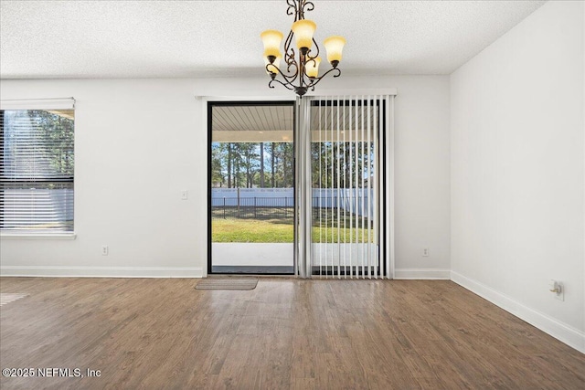 unfurnished room featuring baseboards, a textured ceiling, an inviting chandelier, and wood finished floors