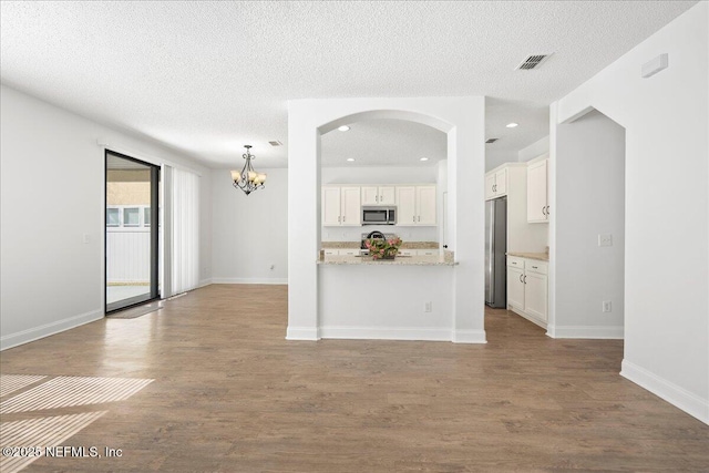 unfurnished living room featuring a notable chandelier, a textured ceiling, baseboards, and wood finished floors