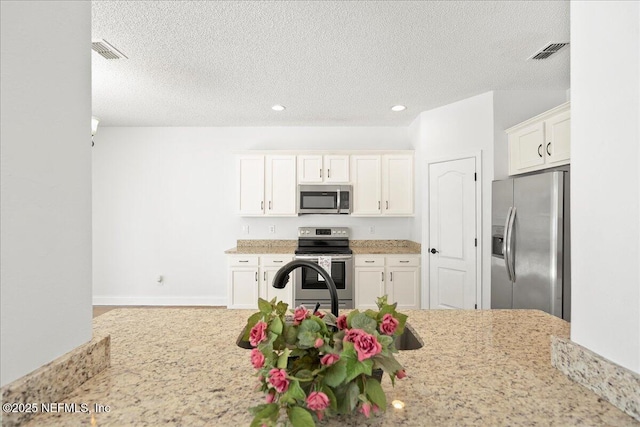 kitchen with light stone counters, visible vents, appliances with stainless steel finishes, and white cabinetry