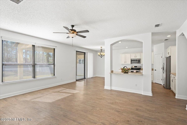 unfurnished living room with baseboards, a textured ceiling, wood finished floors, and ceiling fan with notable chandelier