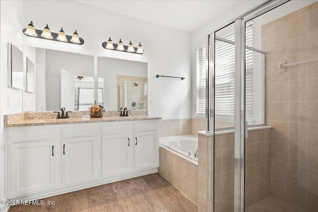 full bath with a stall shower, a sink, wood finished floors, double vanity, and a bath