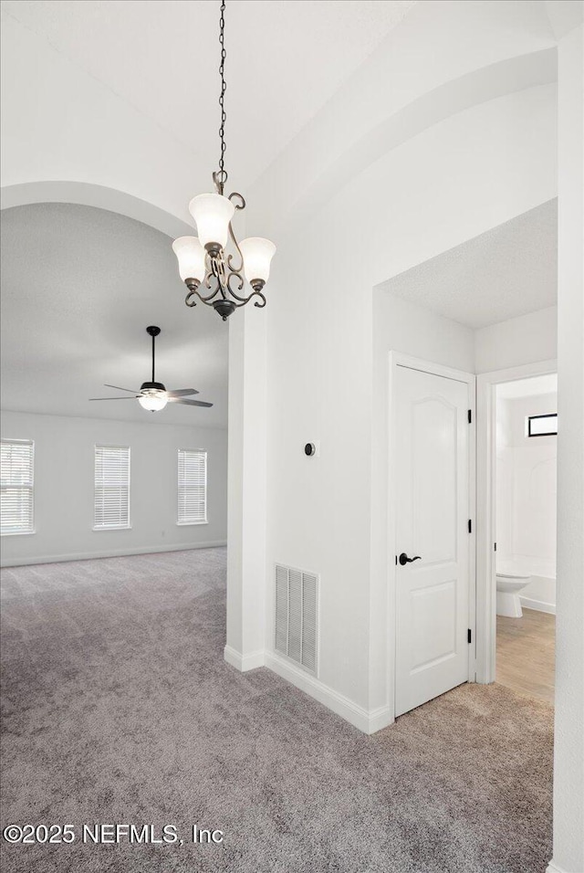 spare room featuring ceiling fan with notable chandelier, carpet, visible vents, and baseboards