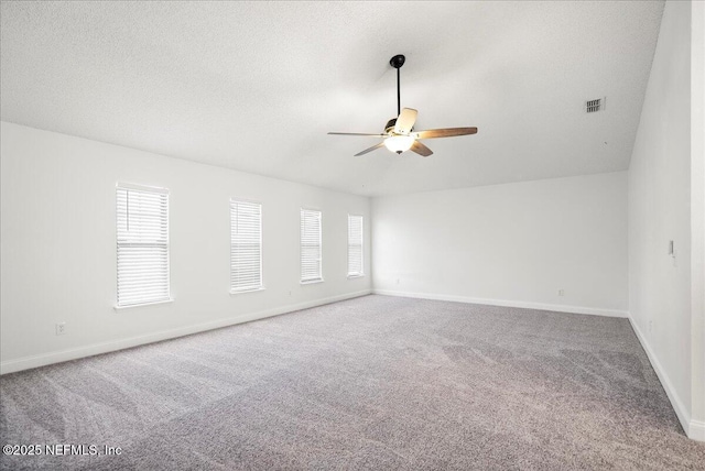 carpeted spare room featuring a wealth of natural light, visible vents, a textured ceiling, and ceiling fan