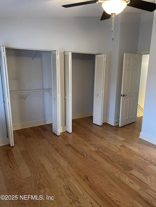 unfurnished bedroom featuring ceiling fan, multiple closets, and light wood-type flooring