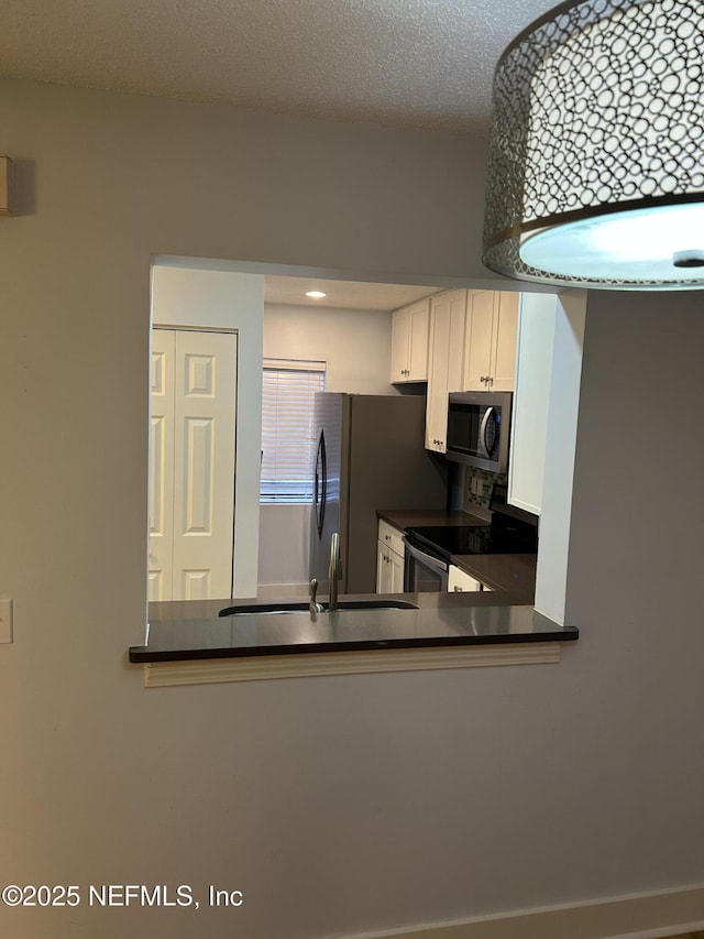 kitchen with appliances with stainless steel finishes, sink, a textured ceiling, and white cabinets