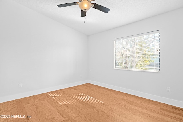 spare room featuring a textured ceiling, light wood finished floors, a ceiling fan, and baseboards