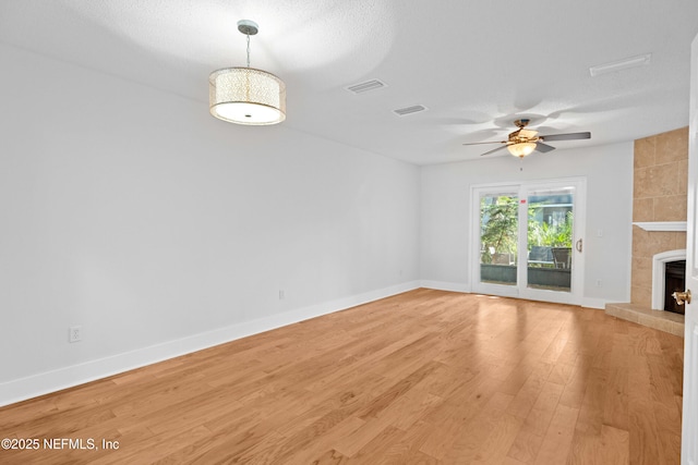 unfurnished living room featuring visible vents, a tiled fireplace, light wood-style flooring, and baseboards