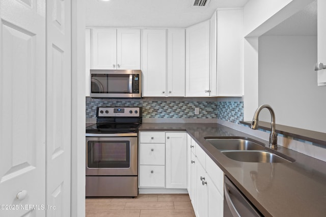 kitchen with appliances with stainless steel finishes, a sink, white cabinetry, and tasteful backsplash