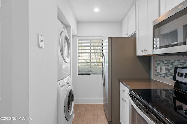 laundry area featuring laundry area, baseboards, stacked washer / dryer, a textured ceiling, and light wood-type flooring