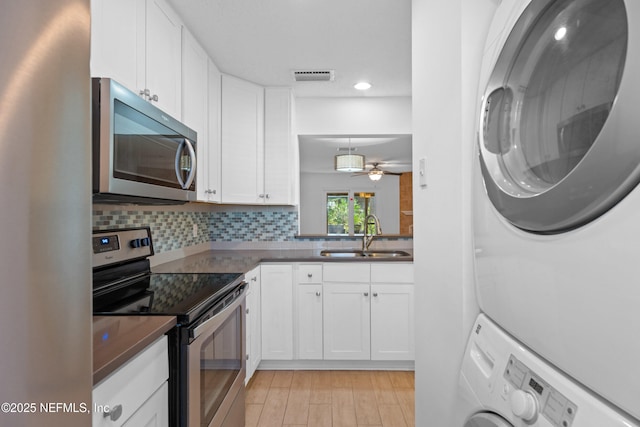 kitchen with stacked washer and clothes dryer, visible vents, decorative backsplash, appliances with stainless steel finishes, and a sink