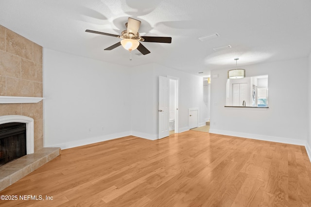 unfurnished living room with light wood finished floors, ceiling fan, a fireplace, and baseboards