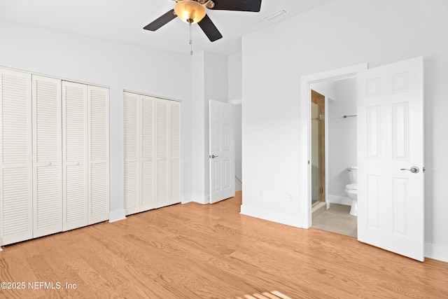 unfurnished bedroom with two closets, visible vents, ensuite bath, wood finished floors, and baseboards