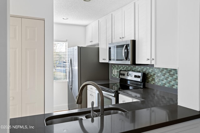 kitchen featuring stainless steel appliances, dark countertops, backsplash, white cabinets, and a sink