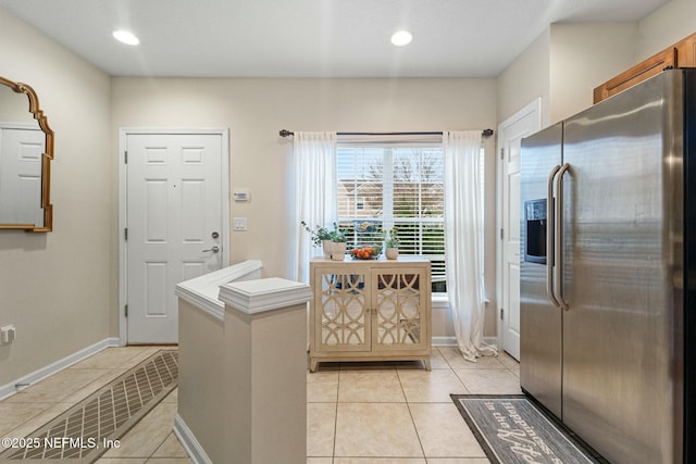 interior space with light tile patterned floors and stainless steel fridge