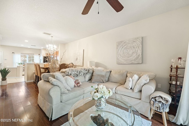 living room featuring a textured ceiling, dark wood-type flooring, and ceiling fan with notable chandelier