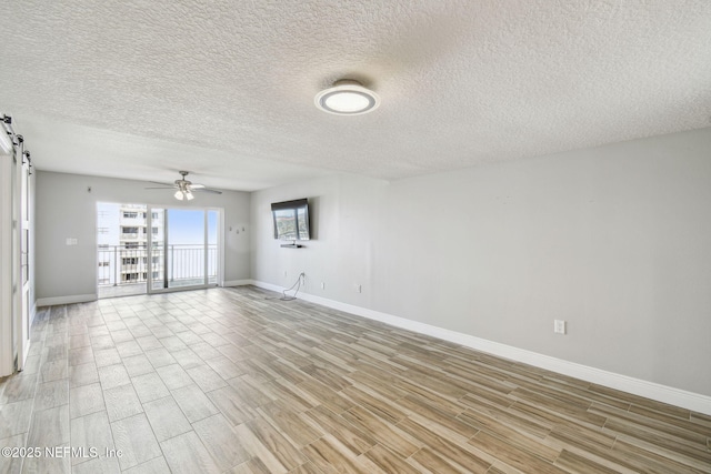 unfurnished room with ceiling fan, a barn door, a textured ceiling, and light hardwood / wood-style floors