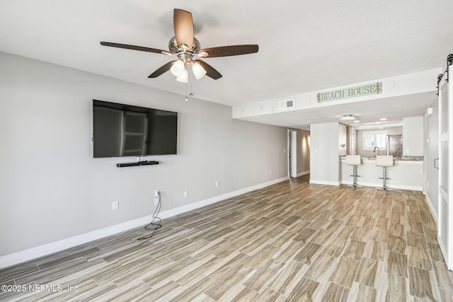 unfurnished living room with sink, light hardwood / wood-style floors, and ceiling fan