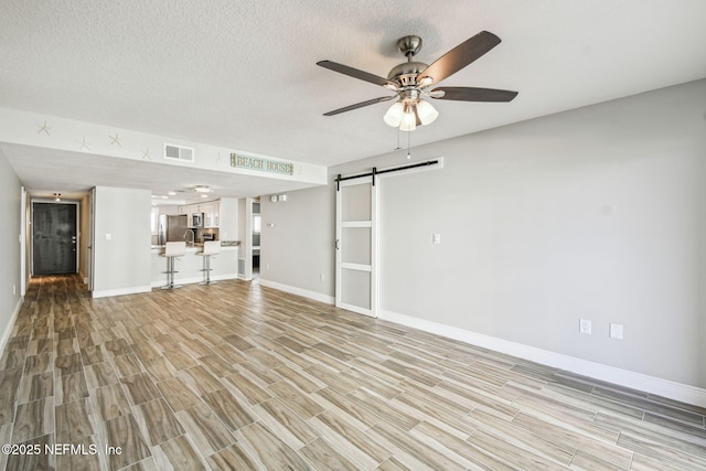 unfurnished living room featuring a barn door, light wood-type flooring, a textured ceiling, and ceiling fan