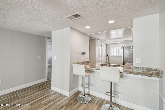 kitchen with sink, a breakfast bar area, light wood-type flooring, stainless steel fridge, and kitchen peninsula