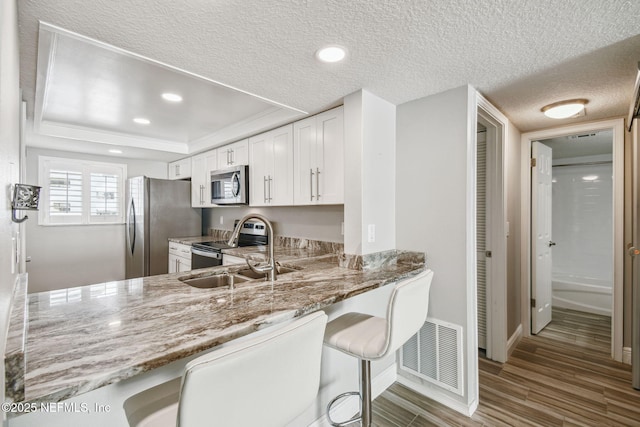 kitchen featuring white cabinets, hardwood / wood-style flooring, light stone counters, stainless steel appliances, and a textured ceiling