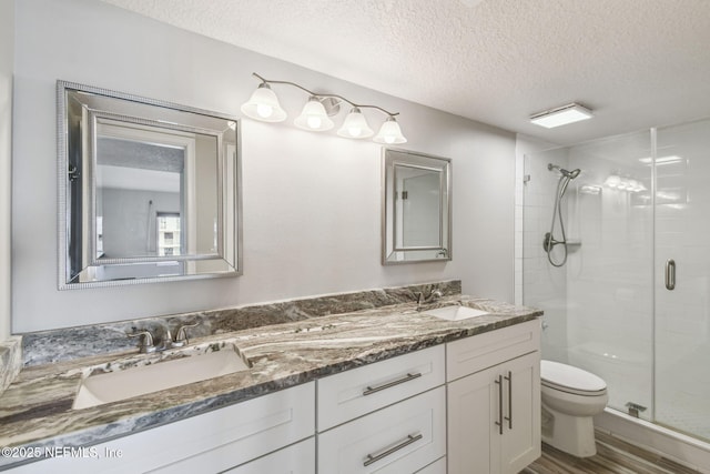 bathroom featuring a textured ceiling, toilet, walk in shower, and vanity