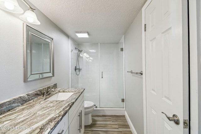 bathroom featuring toilet, hardwood / wood-style flooring, a shower with door, a textured ceiling, and vanity