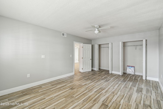 unfurnished bedroom featuring ceiling fan, light hardwood / wood-style flooring, a textured ceiling, and two closets