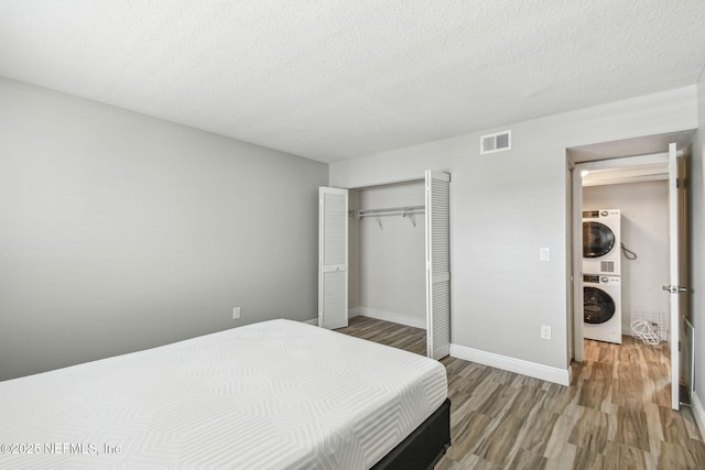 bedroom featuring wood-type flooring, stacked washer / drying machine, a textured ceiling, and a closet