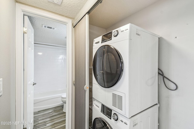 laundry room with a textured ceiling, stacked washer and clothes dryer, and hardwood / wood-style floors