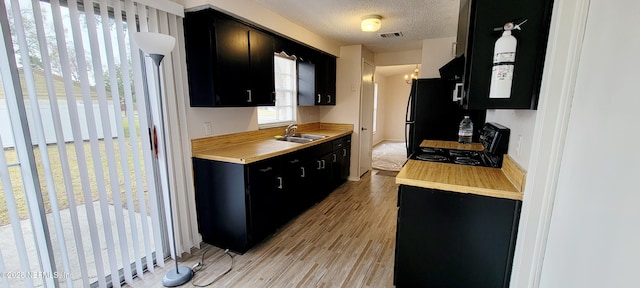 kitchen featuring black refrigerator, sink, stove, light hardwood / wood-style floors, and a textured ceiling