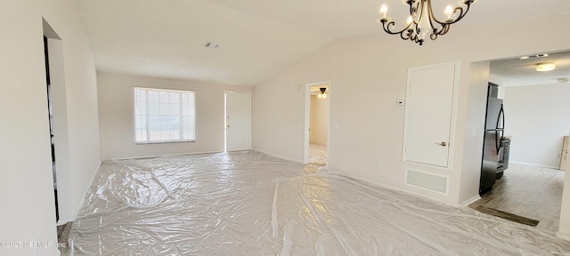 spare room featuring a textured ceiling, vaulted ceiling, and a chandelier