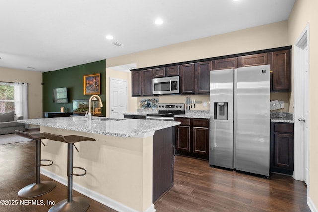 kitchen featuring a kitchen bar, sink, a kitchen island with sink, stainless steel appliances, and dark brown cabinets