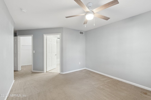 unfurnished bedroom with a spacious closet, light colored carpet, a closet, and ceiling fan