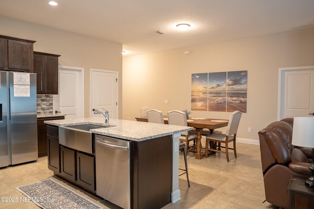 kitchen featuring backsplash, sink, dark brown cabinetry, a kitchen island with sink, and appliances with stainless steel finishes