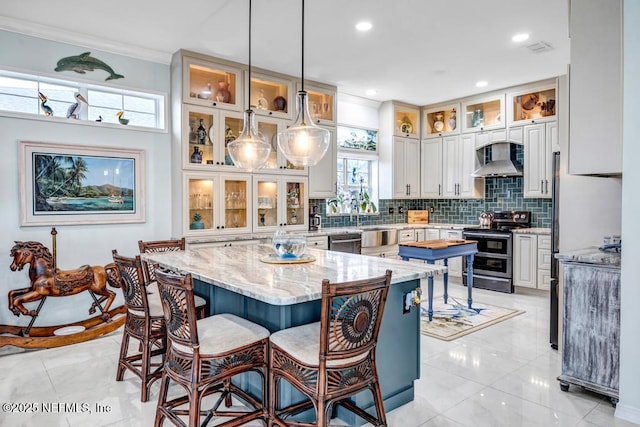 kitchen with wall chimney exhaust hood, appliances with stainless steel finishes, a kitchen island, and white cabinets