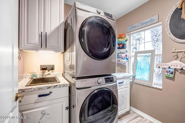 laundry room featuring cabinets, stacked washing maching and dryer, and light hardwood / wood-style flooring