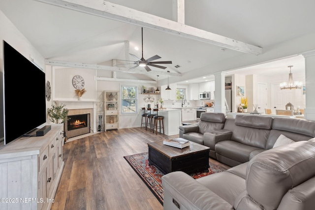 living room with sink, dark wood-type flooring, vaulted ceiling with beams, decorative columns, and ceiling fan with notable chandelier