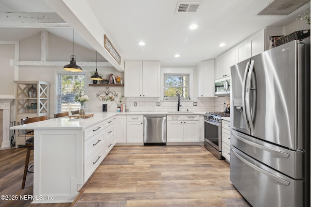 kitchen with a breakfast bar area, white cabinetry, appliances with stainless steel finishes, kitchen peninsula, and pendant lighting