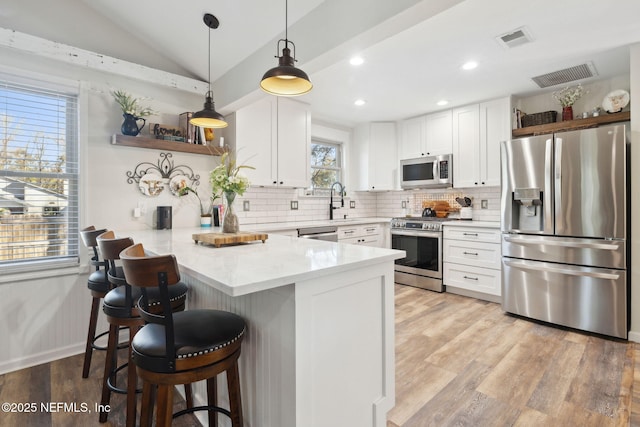 kitchen with lofted ceiling, a kitchen bar, white cabinetry, appliances with stainless steel finishes, and kitchen peninsula