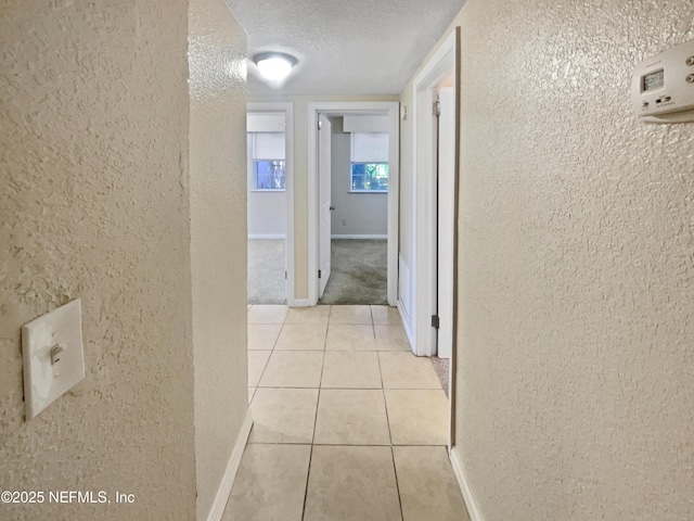 hallway with a textured ceiling and light colored carpet