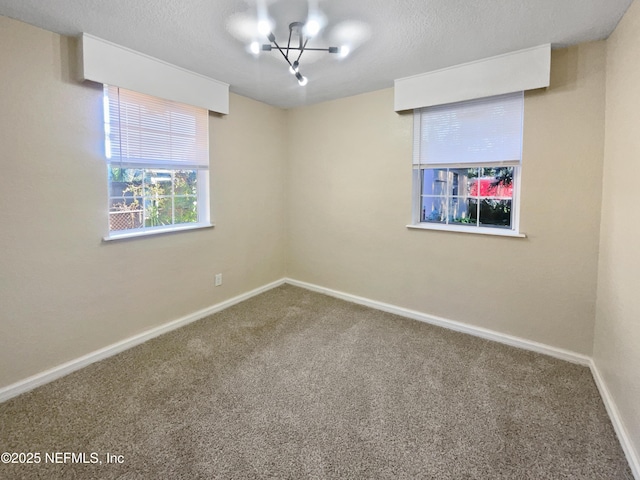 carpeted empty room with a textured ceiling and a notable chandelier