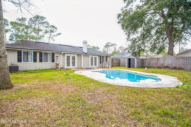 back of property with a storage unit, a yard, central AC unit, a fenced in pool, and french doors