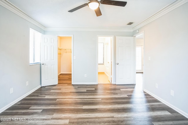 unfurnished bedroom featuring dark hardwood / wood-style flooring, connected bathroom, crown molding, and a walk in closet