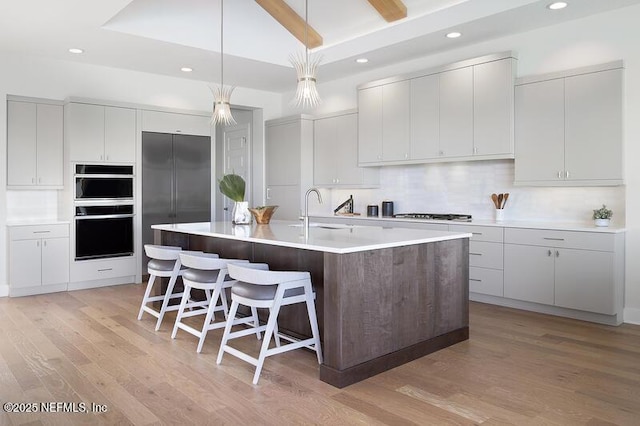 kitchen with pendant lighting, sink, light wood-type flooring, an island with sink, and white cabinets