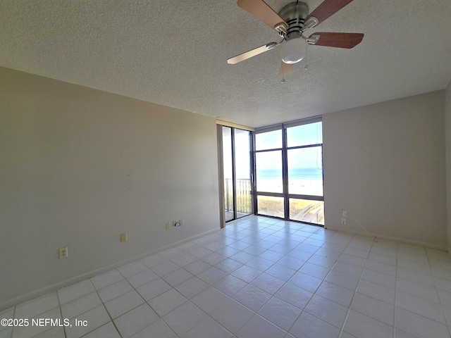 empty room featuring floor to ceiling windows, a water view, a textured ceiling, light tile patterned floors, and ceiling fan