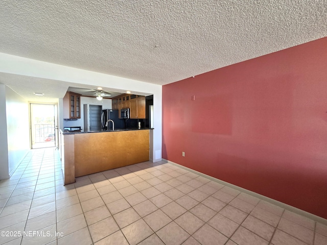 kitchen featuring black refrigerator, kitchen peninsula, a textured ceiling, and light tile patterned floors