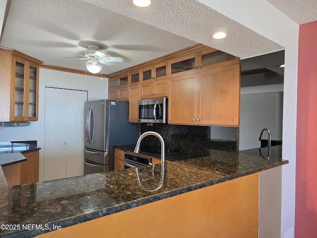 kitchen with ceiling fan, appliances with stainless steel finishes, dark stone countertops, a textured ceiling, and kitchen peninsula